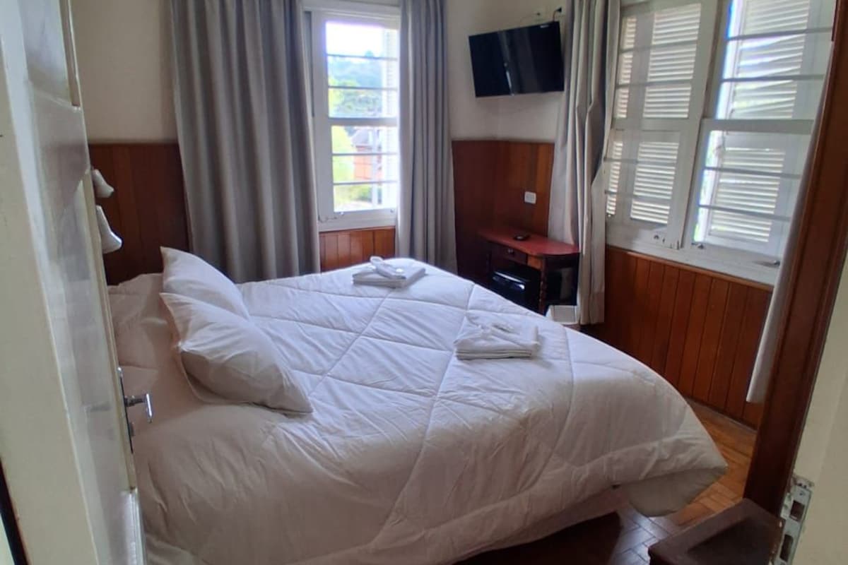 Un dormitorio con una cama grande, televisión de pantalla plana, escritorio y ventana con persianas.