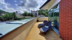 A rooftop terrace with two lounge chairs and a view of a castle in the distance.
