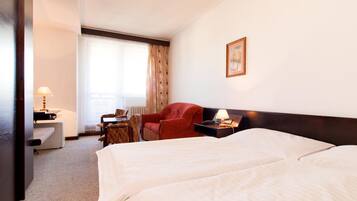 A hotel room with two beds, a desk with a lamp, a red chair, and a window with curtains.