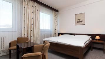 Una camera d'albergo con un letto grande, una scrivania, due sedie, un comodino con una lampada e una finestra con tende.