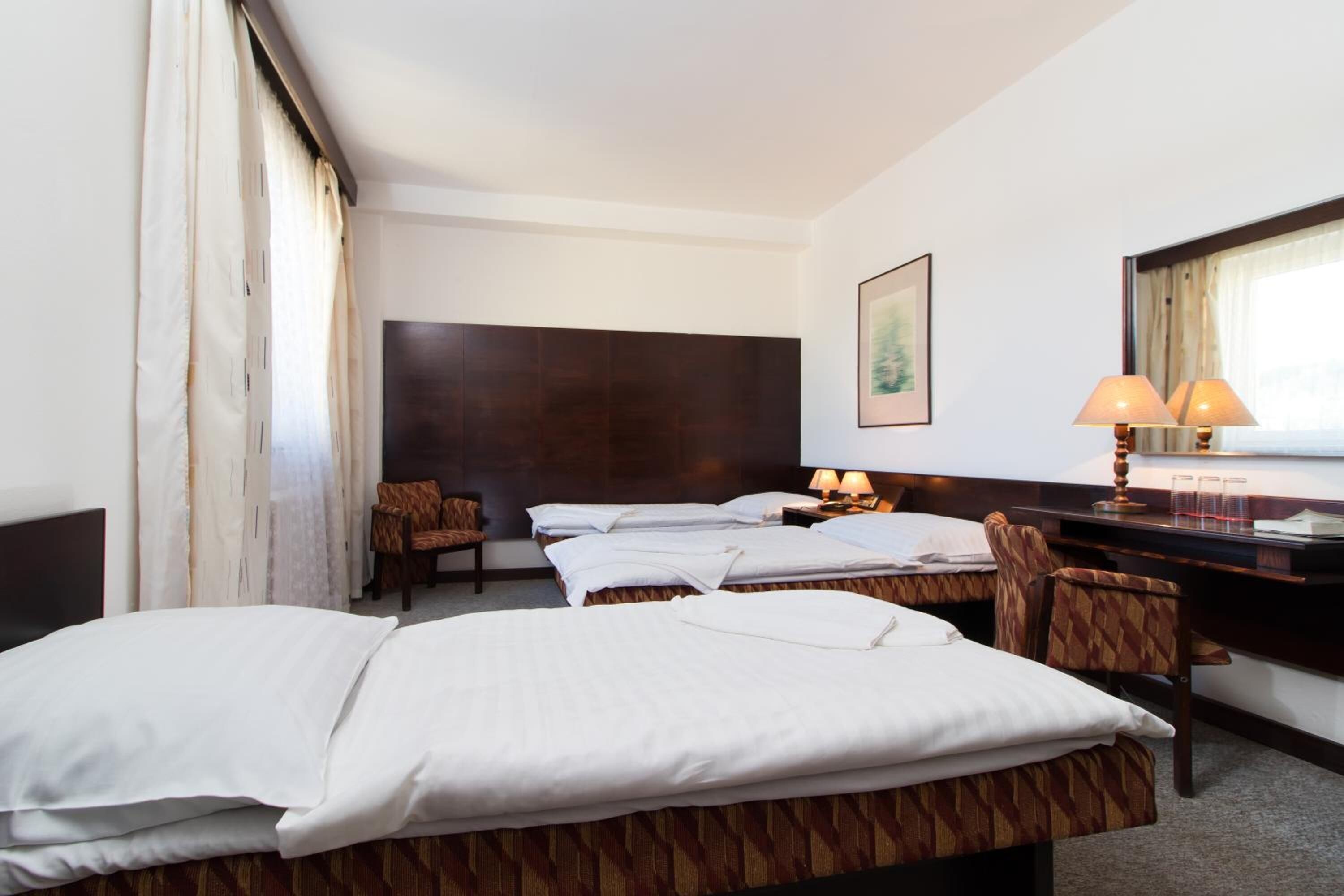 A hotel room with two beds, a desk, a chair, a lamp, and a framed picture on the wall.