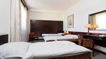 A hotel room with two beds, a desk, a chair, a lamp, and a framed picture on the wall.