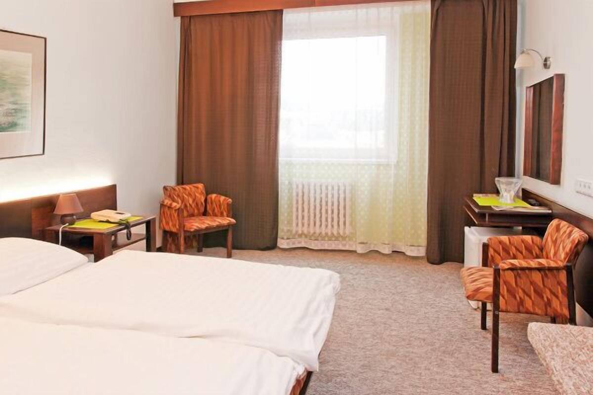 A hotel room with two beds, a desk, a chair, a lamp, and a window with curtains.