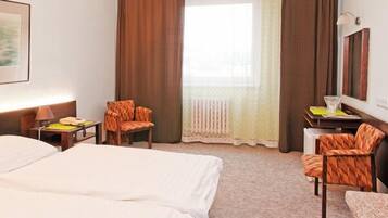 A hotel room with two beds, a desk, a chair, a lamp, and a window with curtains.