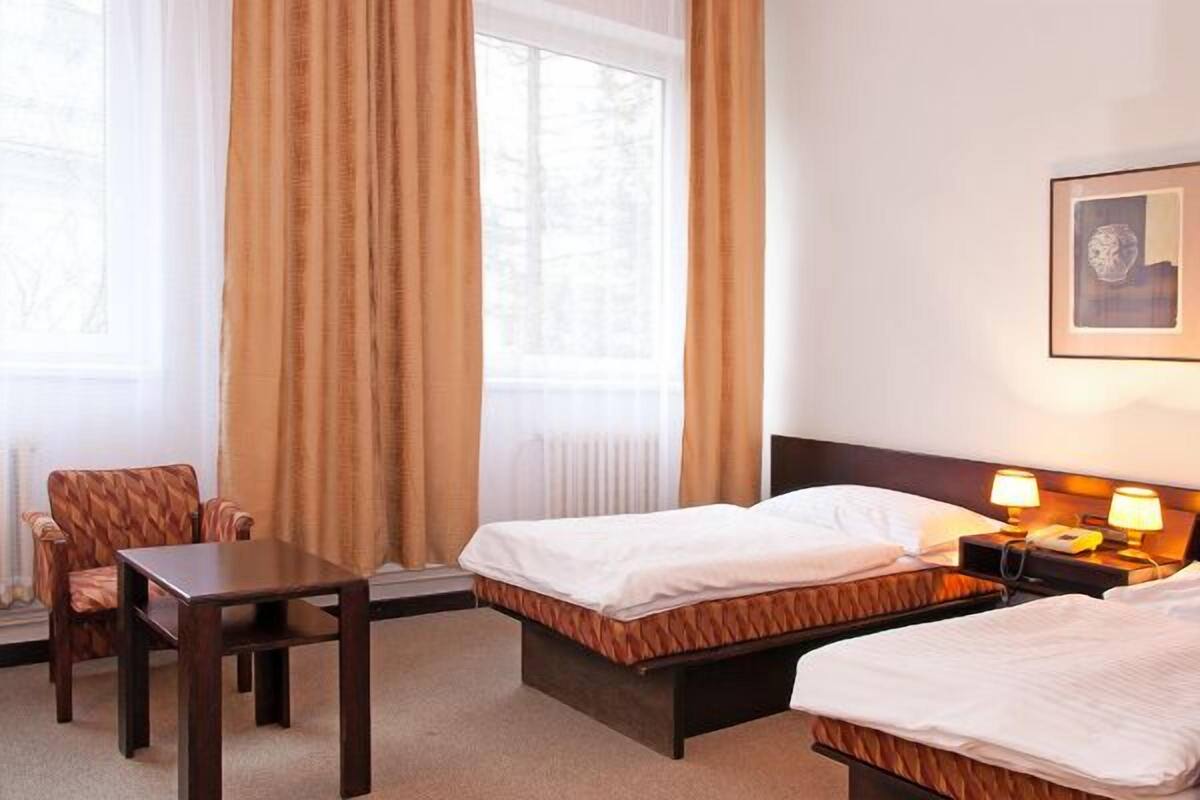 A hotel room with two beds, a wooden table, a chair, and a window with curtains.