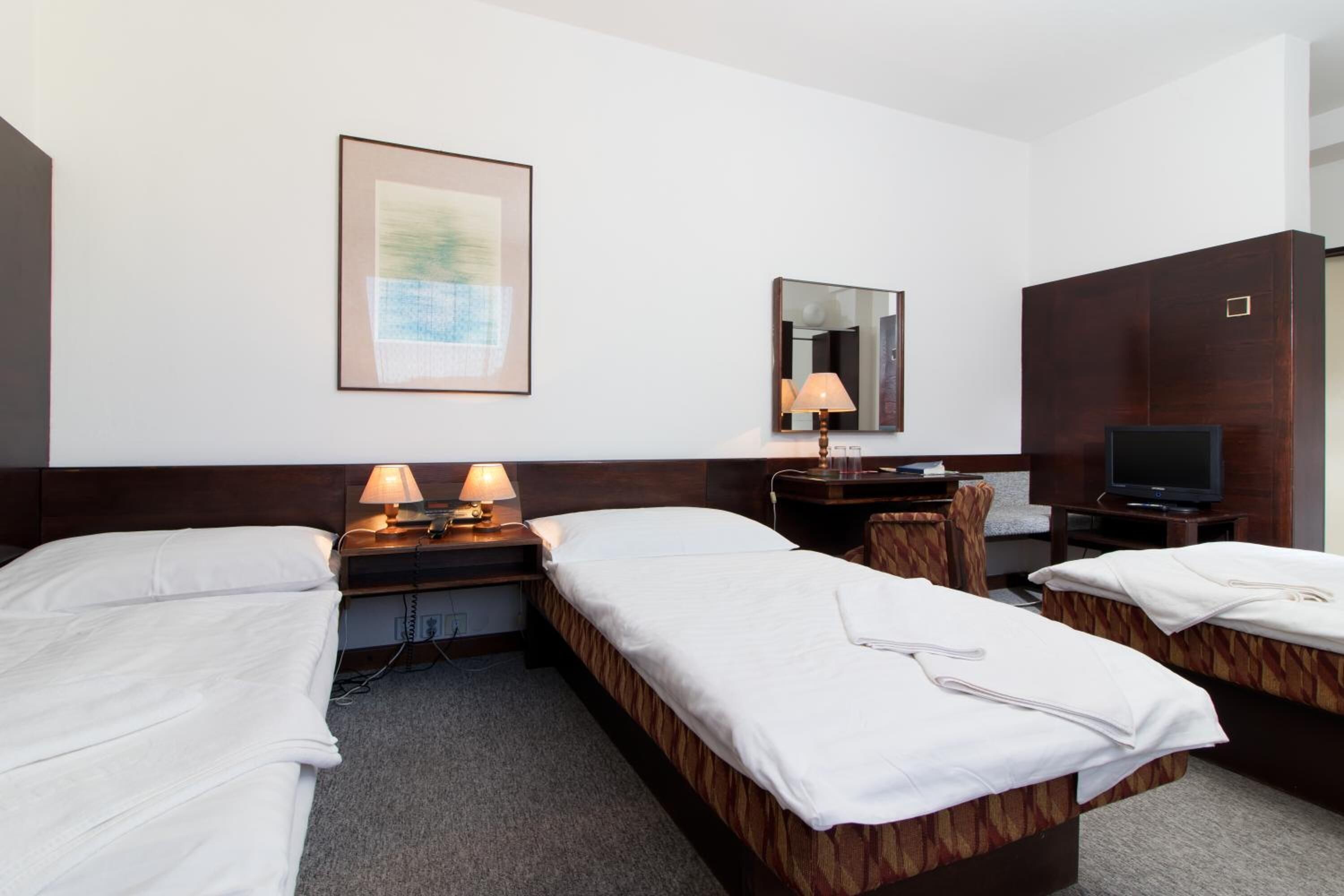Ein Hotelzimmer mit zwei Betten, einem Schreibtisch mit Lampe, einem Fernseher und einem gerahmten Bild an der Wand.