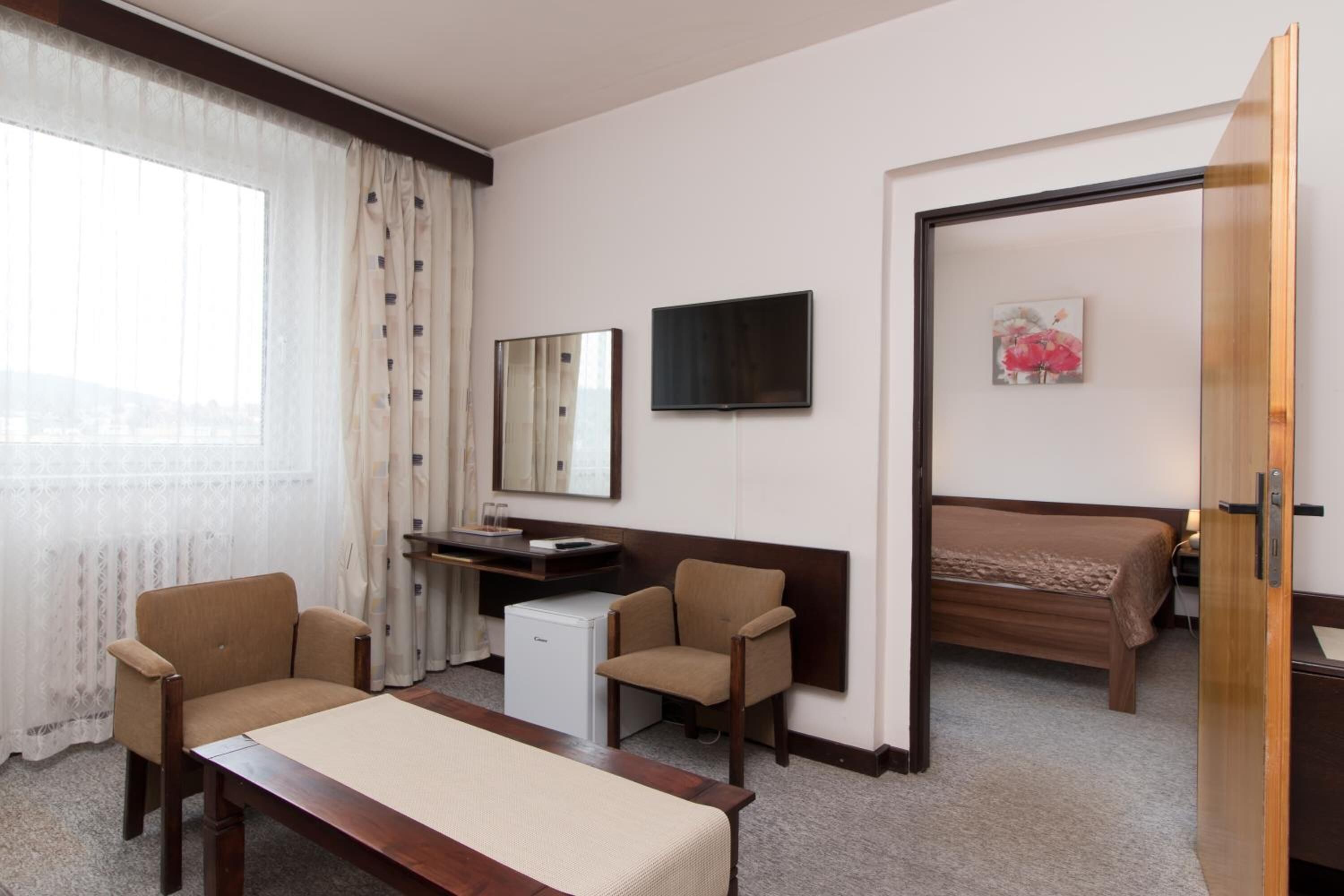 A hotel room with a bed, a desk, two chairs, a television, and a window with curtains.