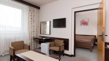 Een hotelkamer met een bed, een bureau, twee stoelen, een televisie en een raam met gordijnen.