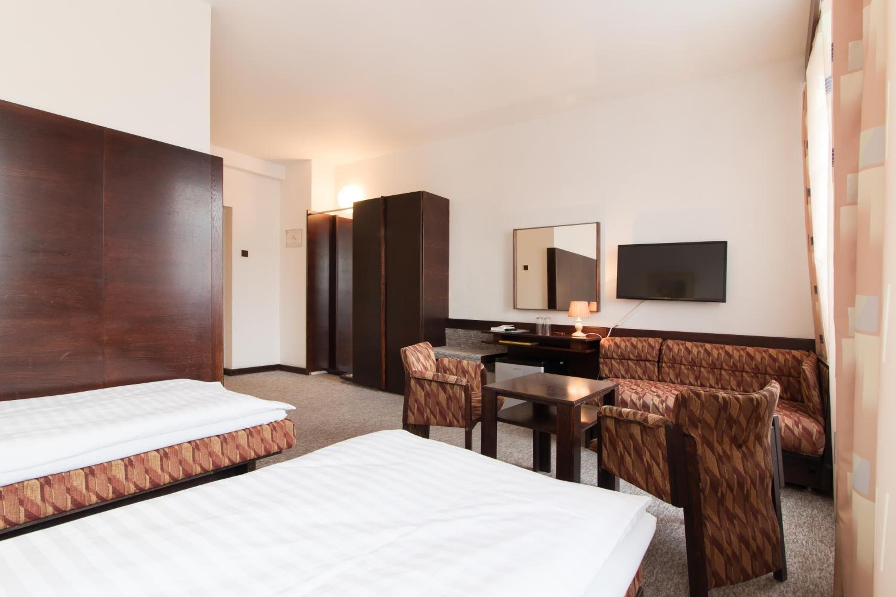 Habitación de hotel con dos camas, un escritorio, una silla, un sofá, un televisor y un espejo.
