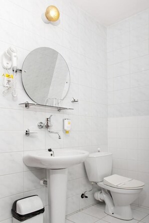 A modern bathroom with a white sink, toilet, and a round mirror.