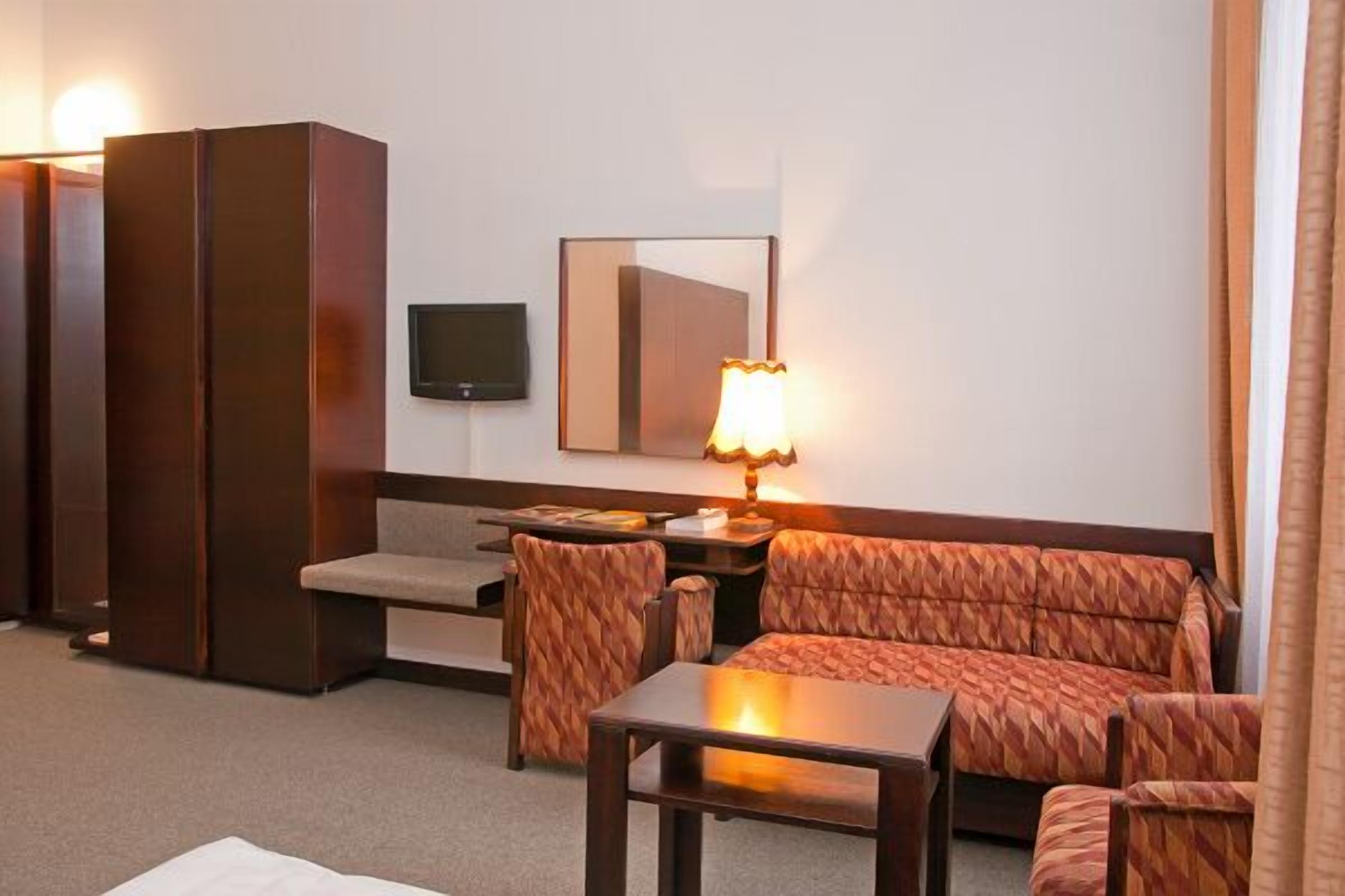 A hotel room with a sofa, armchair, small table, TV, and a lamp.