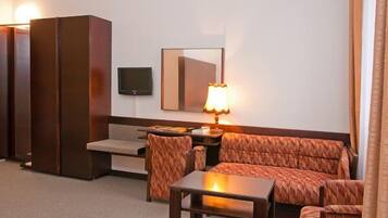 A hotel room with a sofa, armchair, small table, TV, and a lamp.