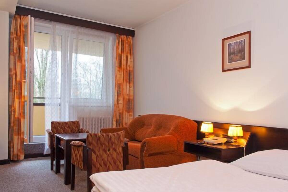 A hotel room with a bed, a desk with two lamps, a chair, and a table.