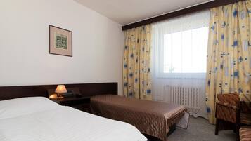 A hotel room with two beds, a nightstand with a lamp, a chair, and a window with curtains.