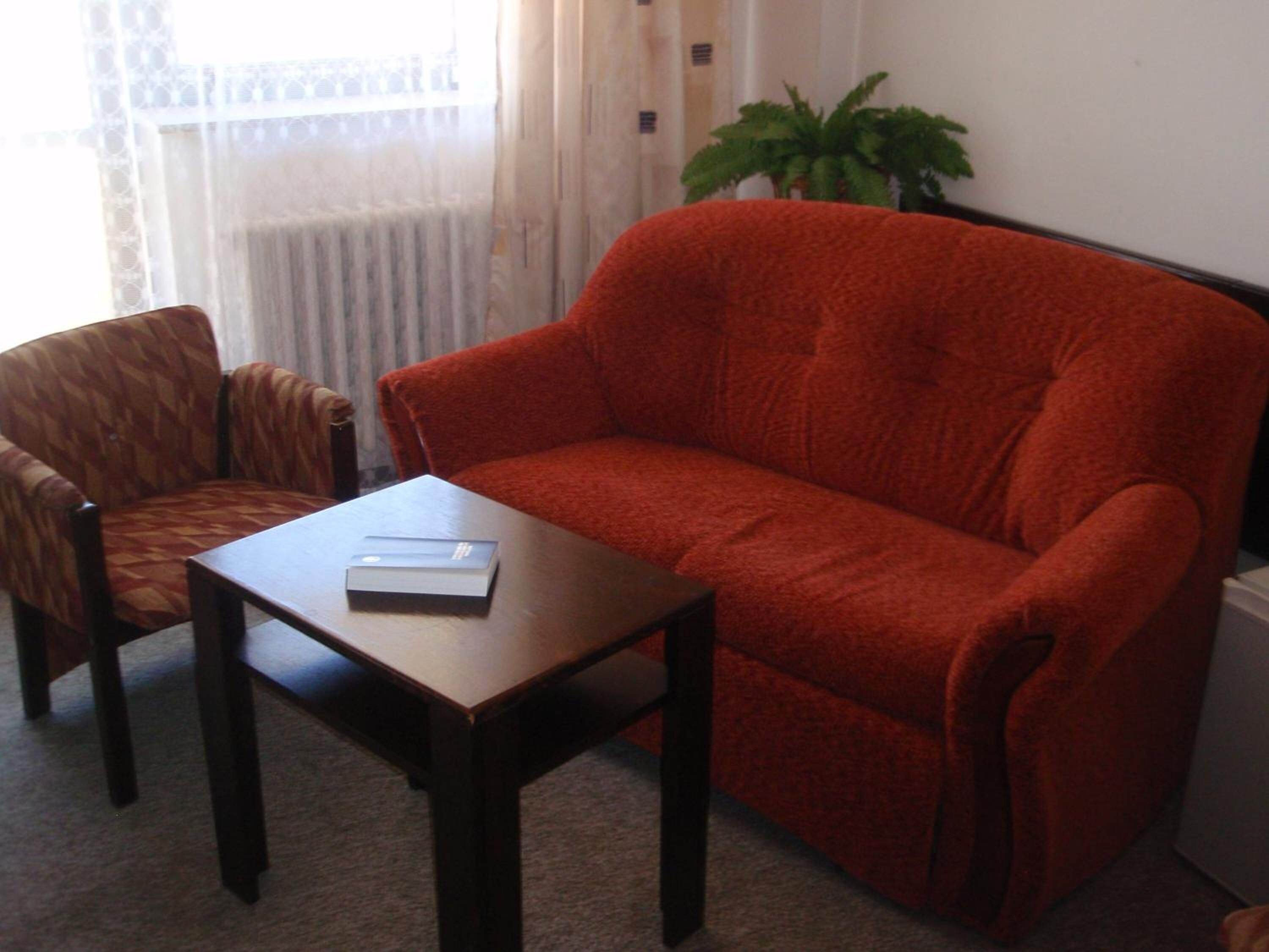 Una sala de estar con un sofá rojo, un sillón estampado y una pequeña mesa con un libro.