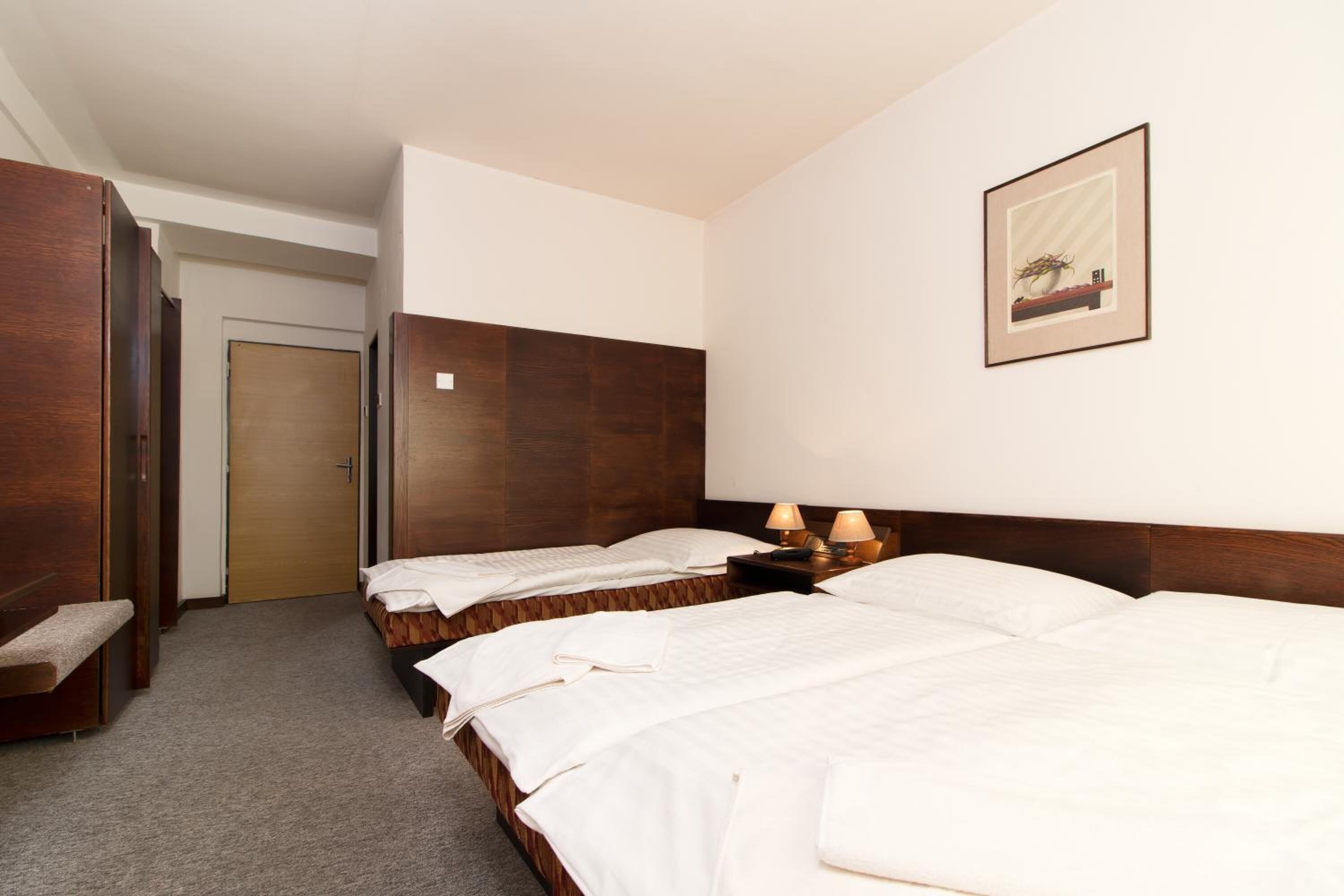 Ein Hotelzimmer mit zwei Betten, einem hölzernen Kopfteil, einem gerahmten Bild an der Wand und einer Tür zu einem anderen Raum.