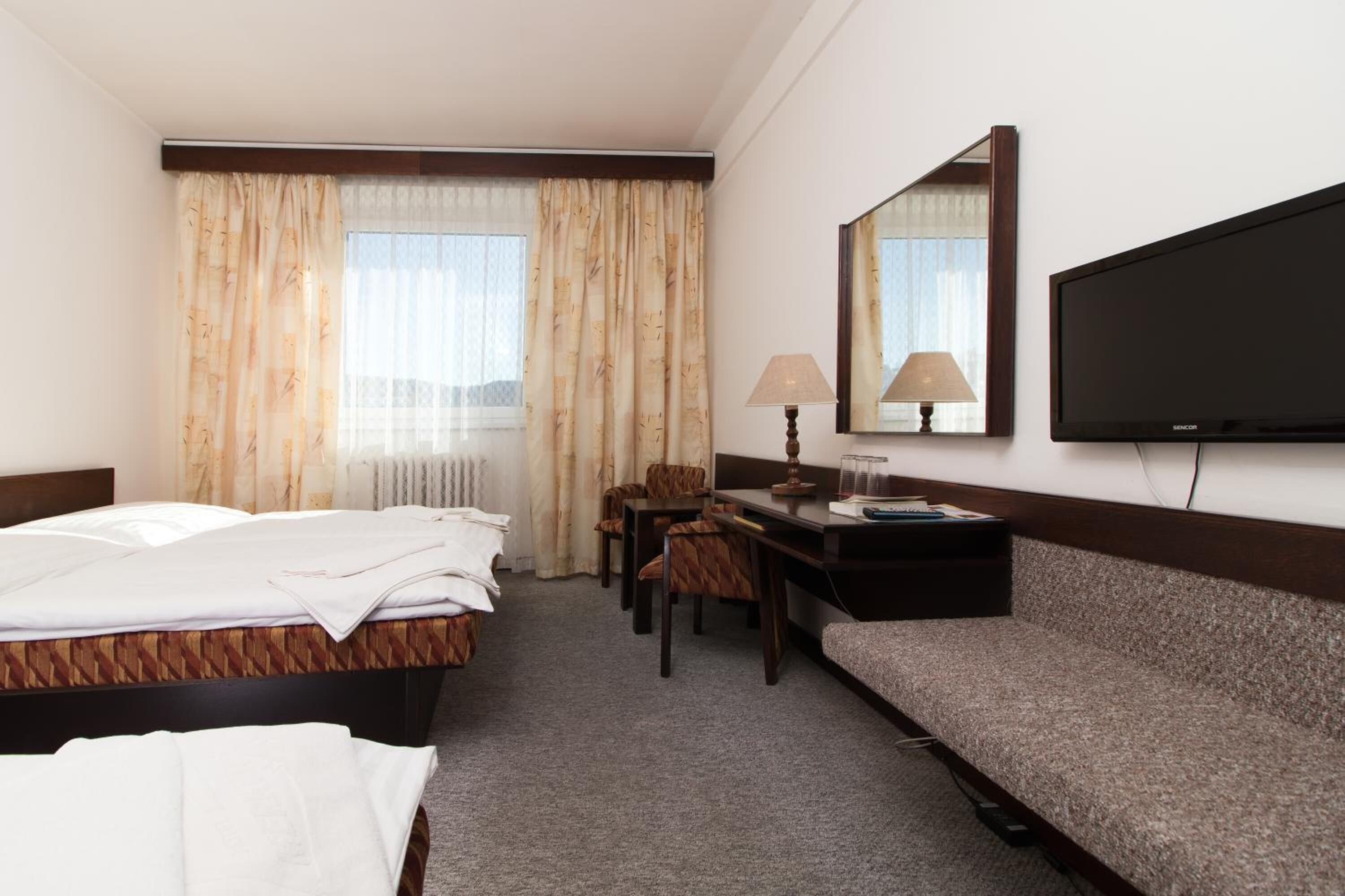 Habitación de hotel con dos camas, un escritorio, una silla, un sofá, un televisor y una ventana con cortinas.