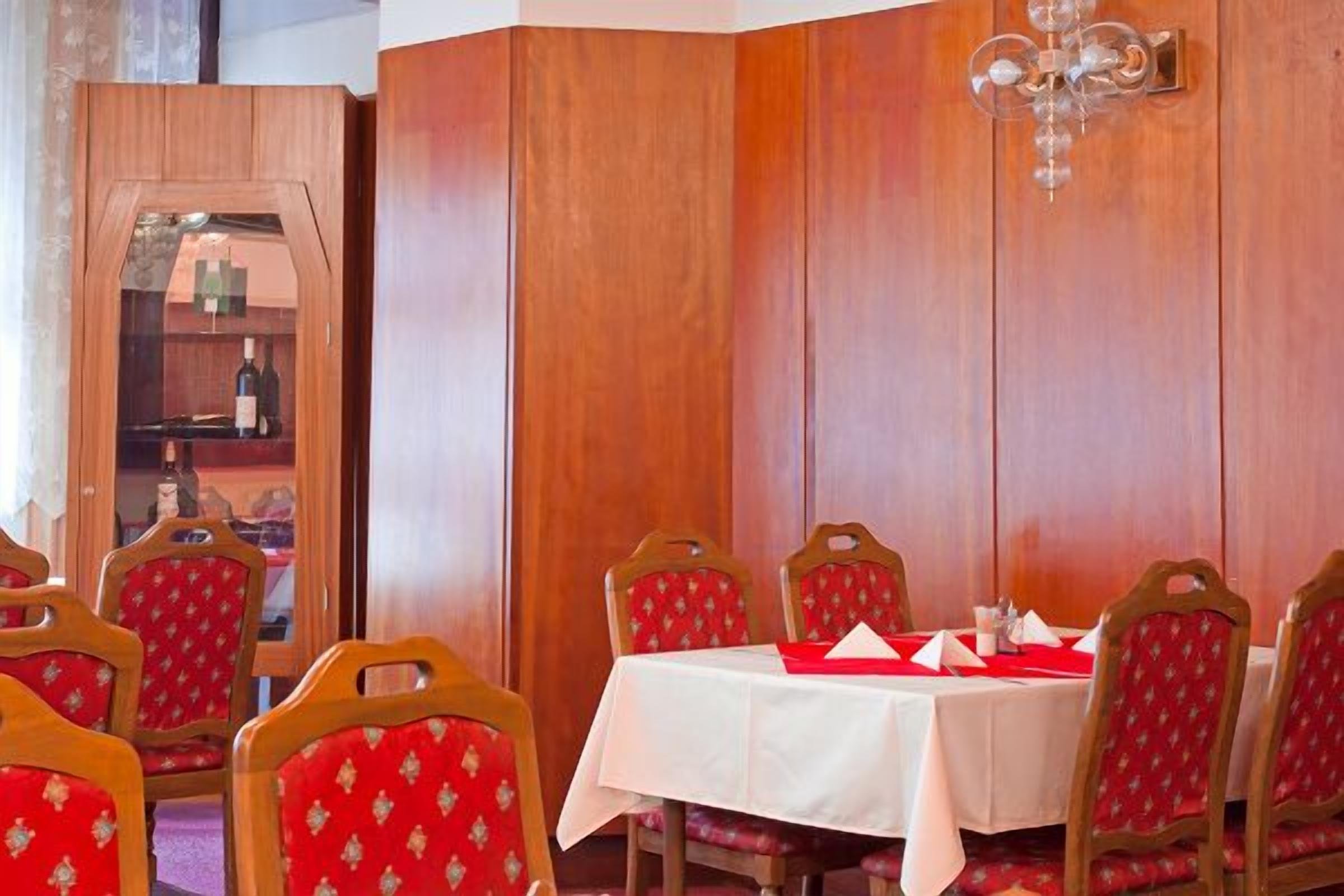A dining area with wooden paneling, a chandelier, and red upholstered chairs.