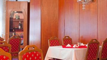 A dining area with wooden paneling, a chandelier, and red upholstered chairs.