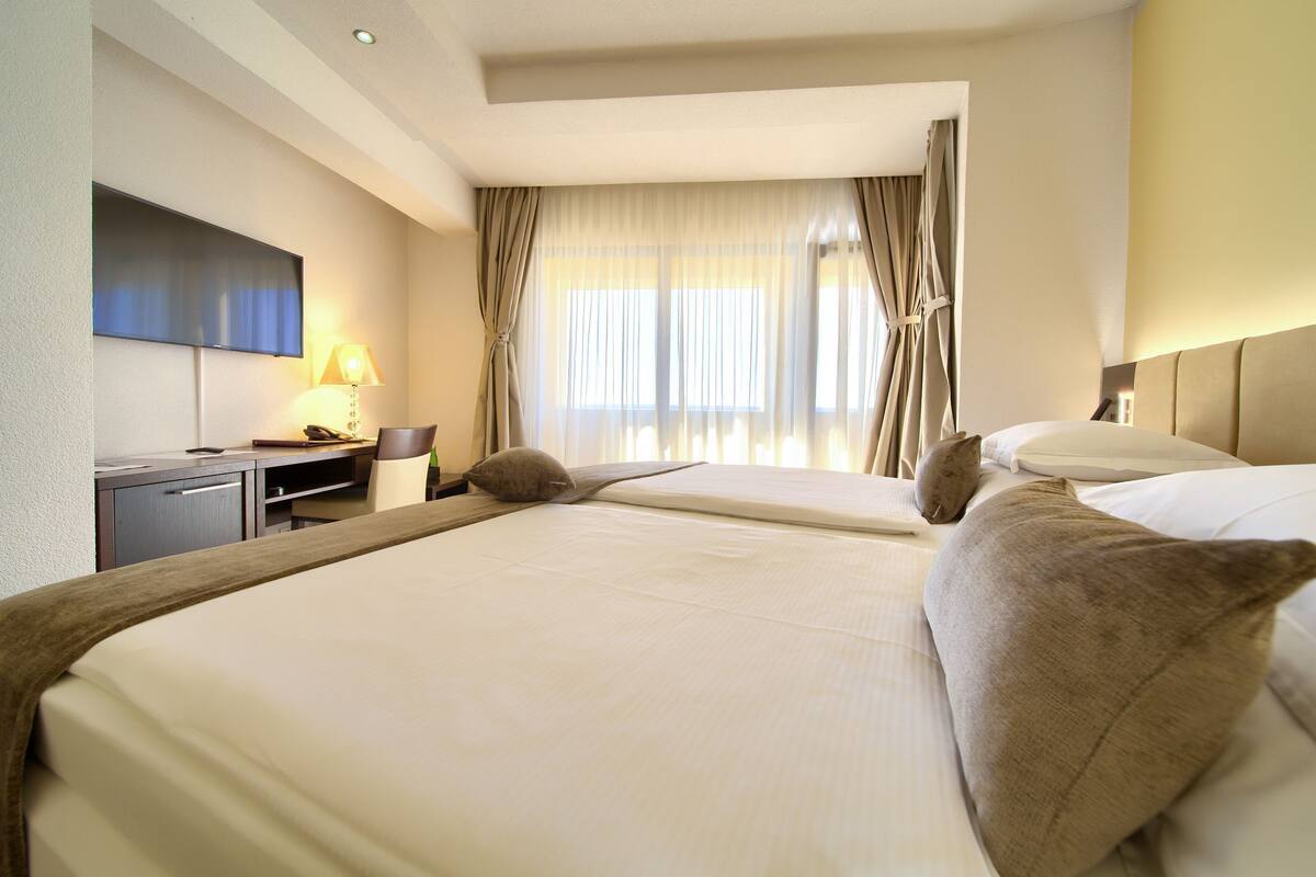 Een hotelkamer met twee bedden, een bureau met lamp, een televisie en een raam met gordijnen.