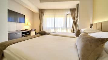 Habitación de hotel con dos camas, un escritorio con lámpara, televisión y ventana con cortinas.