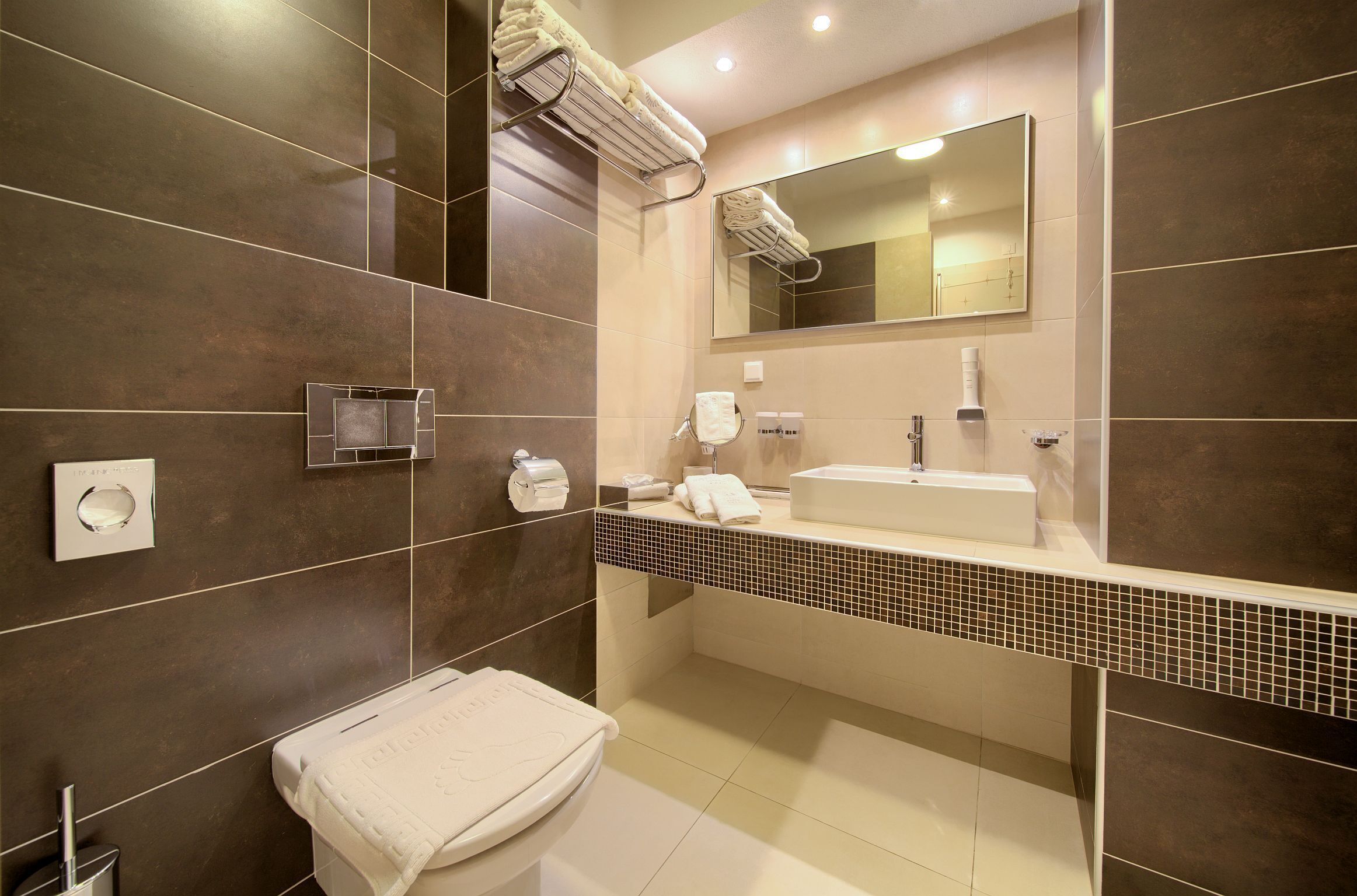 A modern bathroom with a large mirror, a sink, and a toilet.