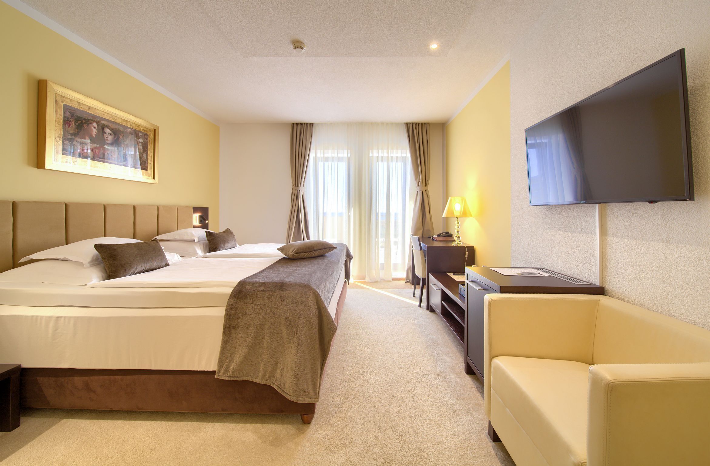 A hotel room with two beds, a desk, a TV, and a couch.