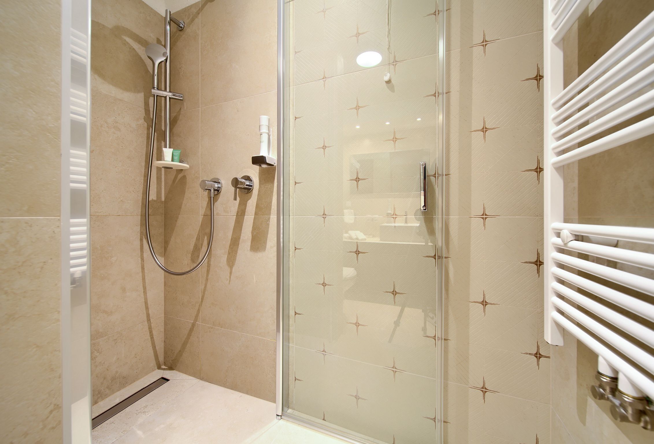 A modern bathroom with a glass shower enclosure, a white towel rack, and a small shelf with toiletries.