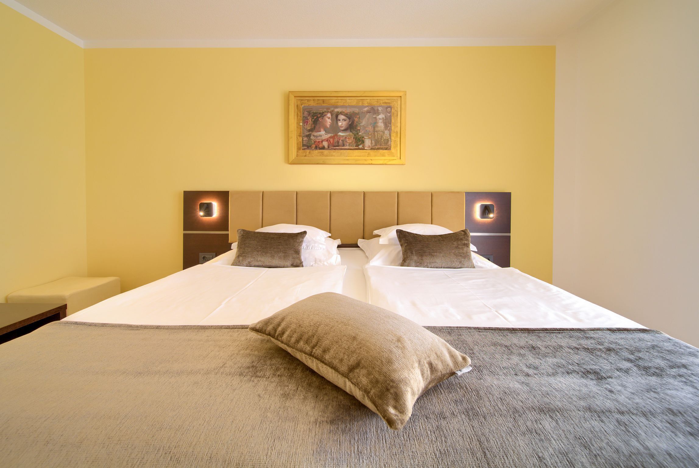 Cama doble con dos almohadas, cabecera con iluminación integrada y una obra de arte enmarcada encima.