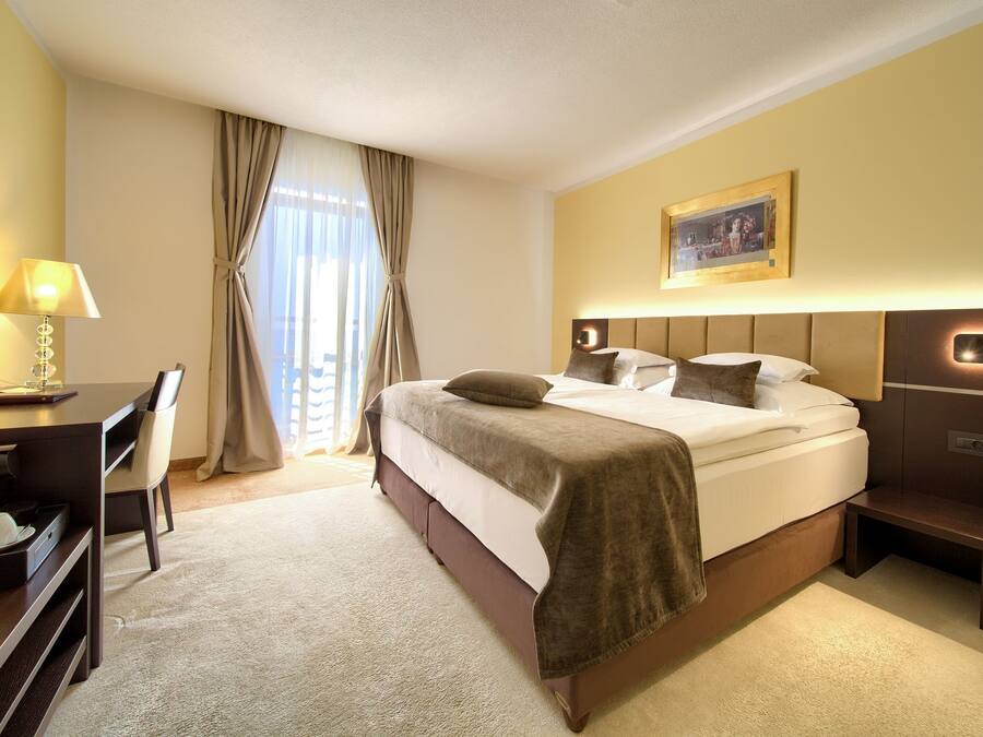 A hotel room with a bed, desk, chair, lamp, and a painting on the wall.