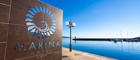 Señal de hotel con vista al puerto deportivo, logotipo y nombre, con una vista tranquila del agua y cielo despejado.