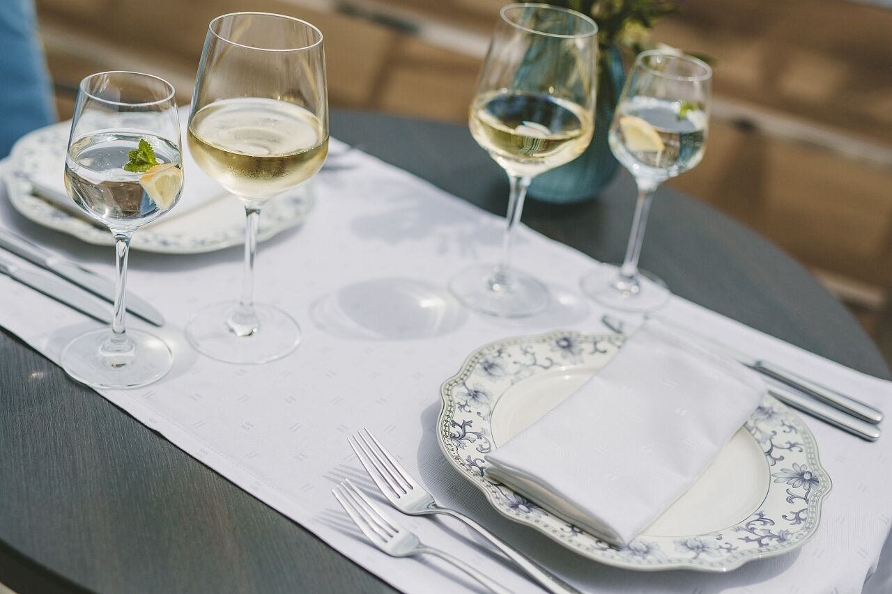 A table set with white plates, clear wine glasses, and silverware.