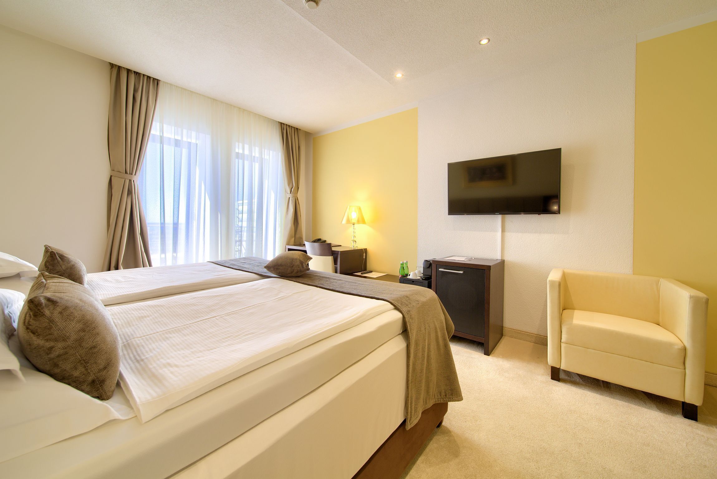 Ein Hotelzimmer mit einem großen Bett, einem an der Wand montierten Fernseher, einem Schreibtisch und einem Sofa.