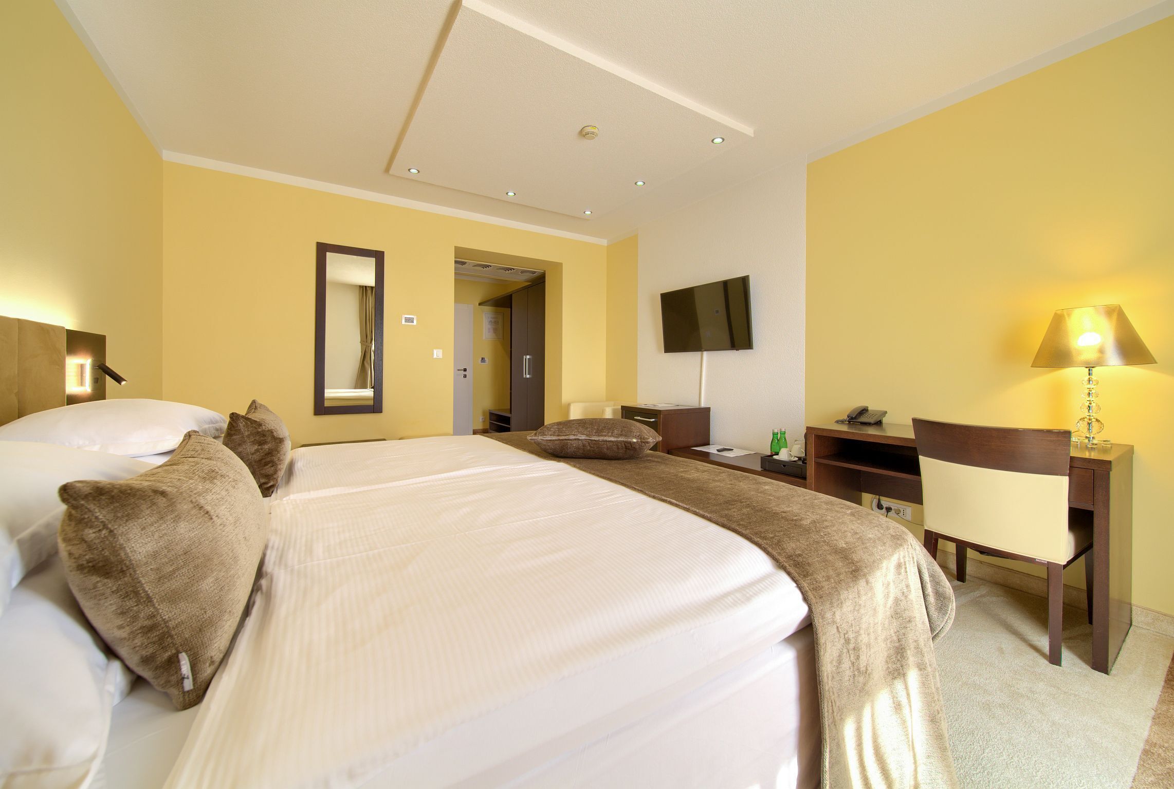 A hotel room with a large bed, a desk, a chair, a TV, and a mirror.