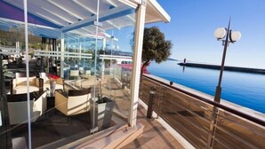 Un área de estar al aire libre con paredes de vidrio y vista al mar y a un muelle.