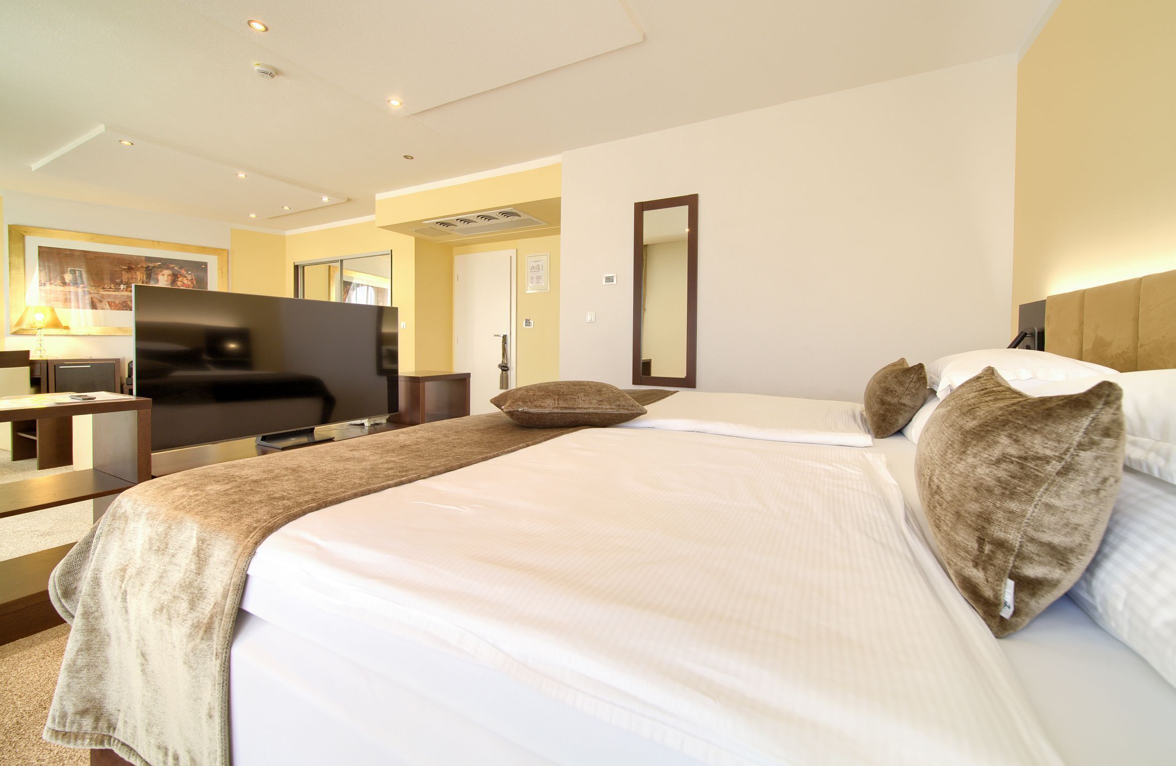 A hotel room with a bed, a television, a desk, and a mirror.