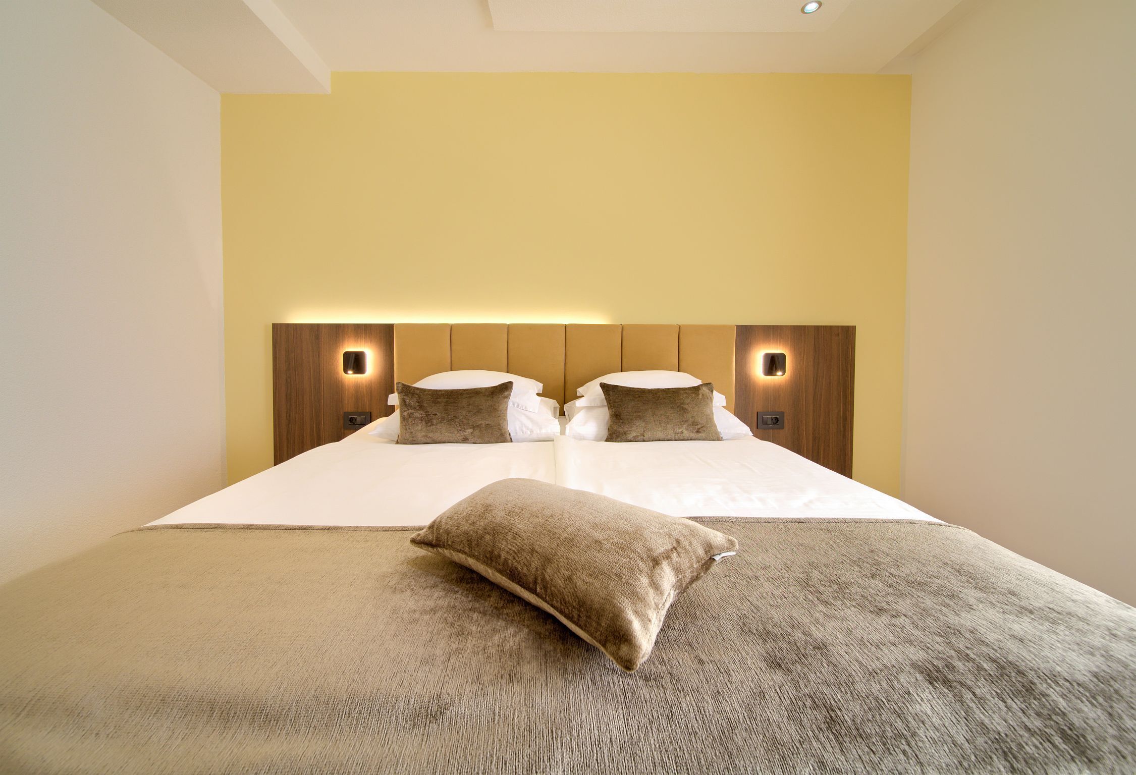 Una habitación de hotel con una cama grande, dos almohadas, cabecero con iluminación integrada y piso alfombrado.