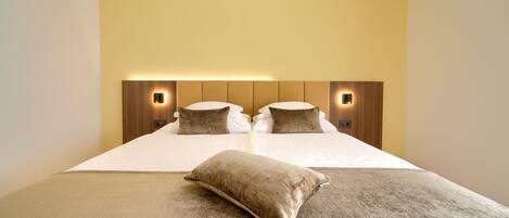 Una habitación de hotel con una cama grande, dos almohadas, cabecero con iluminación integrada y piso alfombrado.