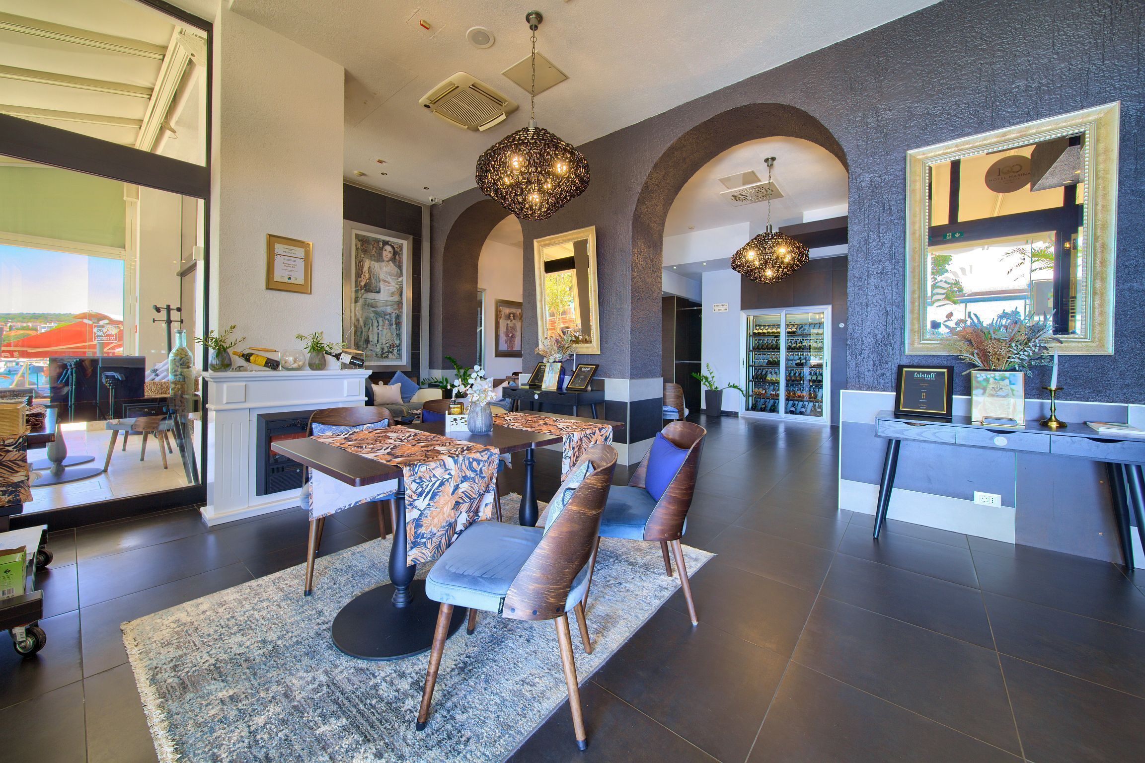 A spacious living area with a fireplace, dining table, and chairs, a kitchen area with a refrigerator, and a large mirror reflecting the room.