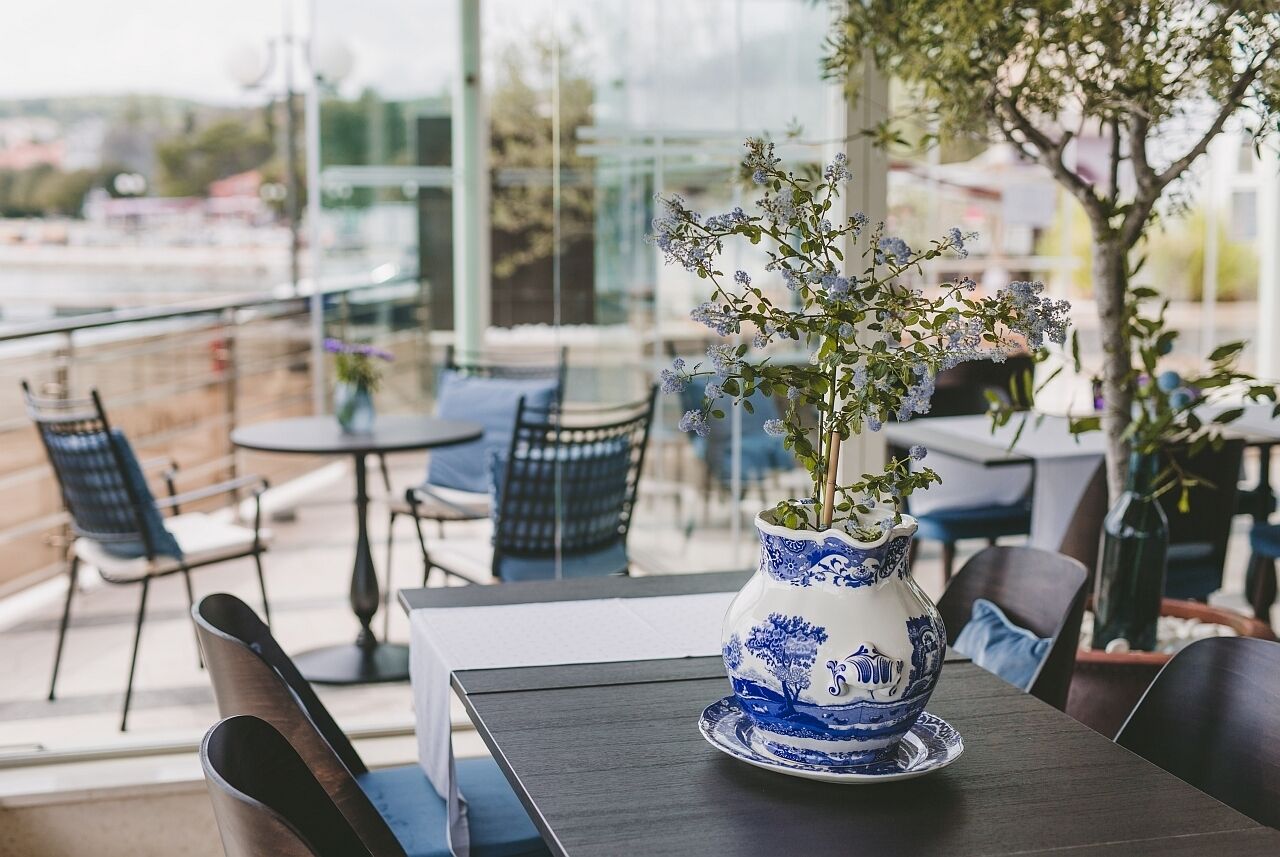 A table with a blue and white vase containing a plant, surrounded by chairs and a glass railing.