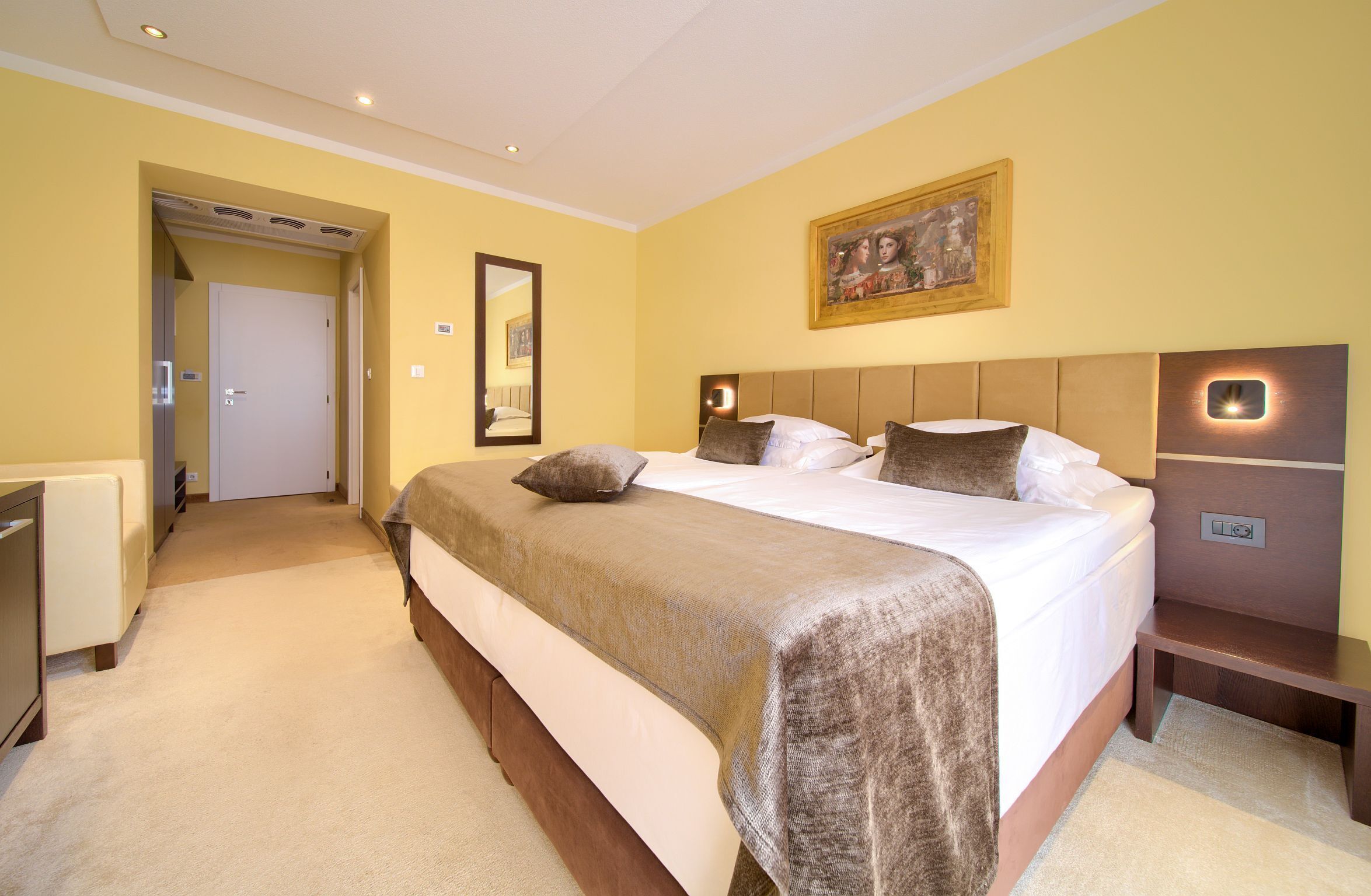 A hotel room with a large bed, bedside tables, a mirror, and a painting on the wall.