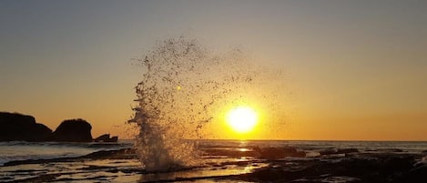 Un atardecer sobre una playa rocosa con olas rompiendo en la orilla.