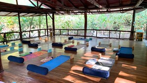 An indoor yoga studio with wooden flooring, blue yoga mats, and cushions arranged for practice. - Nosara B&B Retreat (Nosara)