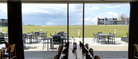 A restaurant with a view of a grassy field and buildings in the distance. Tables and chairs are arranged for dining.