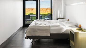 Un dormitorio moderno con una cama grande, una mesita de noche de madera y vistas a un campo cubierto de hierba a través de una puerta corredera.