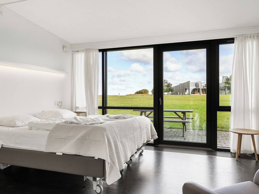 Un dormitorio moderno con una cama grande, un escritorio y vista a un área verde a través de una puerta corrediza.