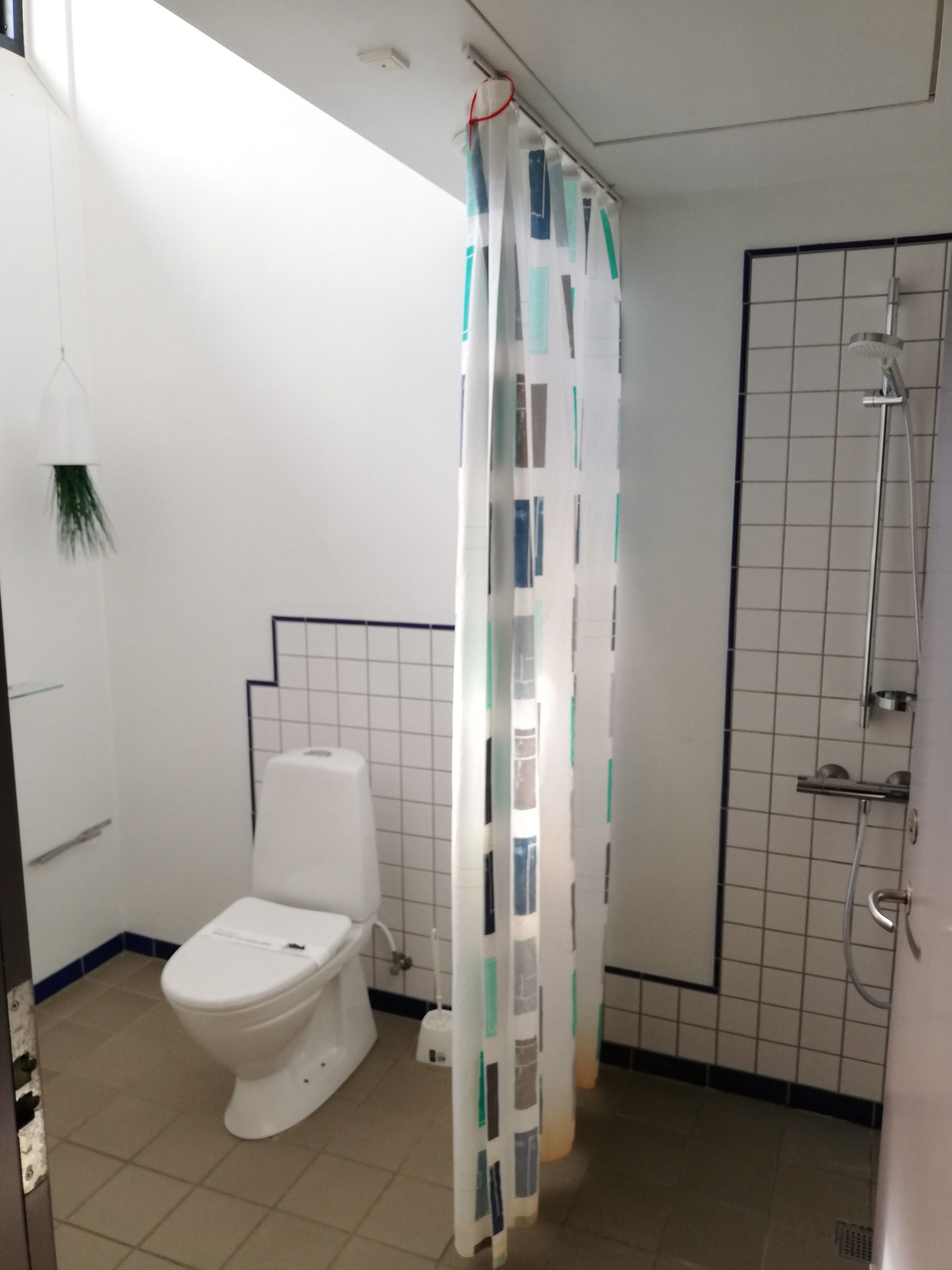 Et badeværelse med toilet, bruser og et gardin med et geometrisk mønster.