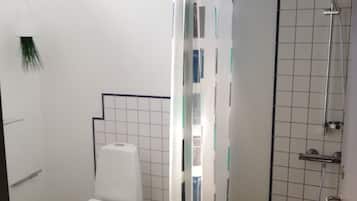 Et badeværelse med toilet, bruser og et gardin med et geometrisk mønster.