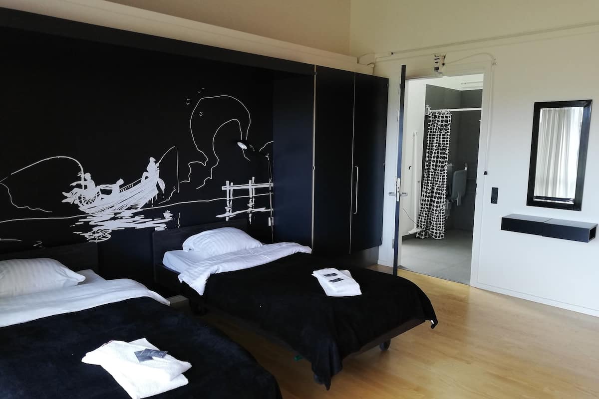 Une chambre d’hôtel avec deux lits, une fresque murale en noir et blanc, un miroir et une porte donnant sur une salle de bain.