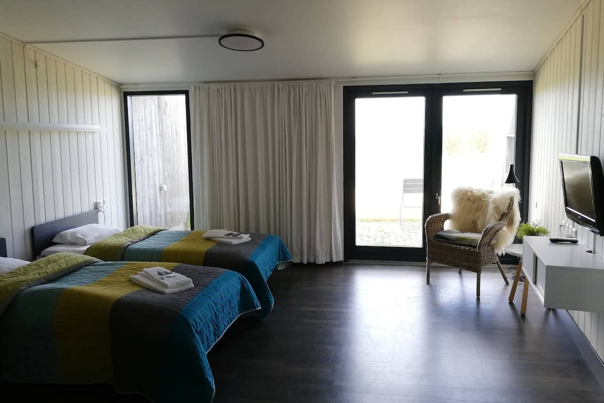Une chambre d’hôtel avec deux lits, une chaise, un bureau avec un ordinateur et une grande fenêtre.
